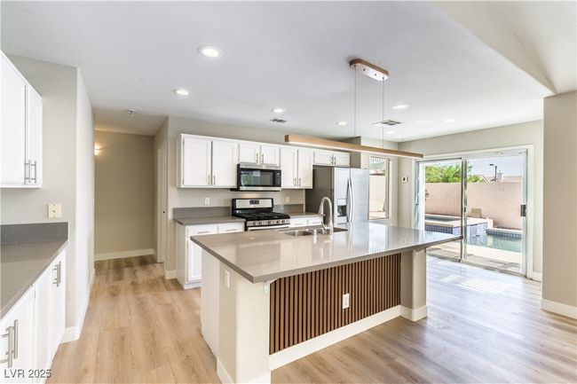 Kitchen featuring stainless steel appliances, a sink, light wood finished floors, a center island with sink, and recessed lighting | Image 7