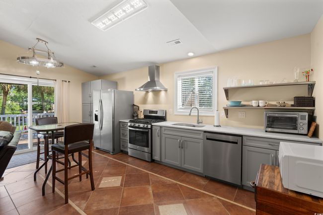 Kitchen featuring stainless steel appliances, a sink, wall chimney exhaust hood, gray cabinetry, and vaulted ceiling | Image 20