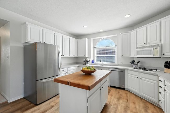 Kitchen featuring stainless steel appliances, light wood finished floors, wood counters, a kitchen island, and white cabinetry | Image 14