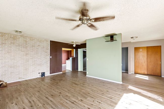 Unfurnished living room with light wood finished floors, brick wall, ceiling fan, baseboards, and a textured ceiling | Image 18