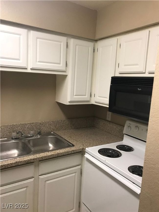 Kitchen with white range with electric cooktop, black microwave, white cabinetry, and a sink | Image 4