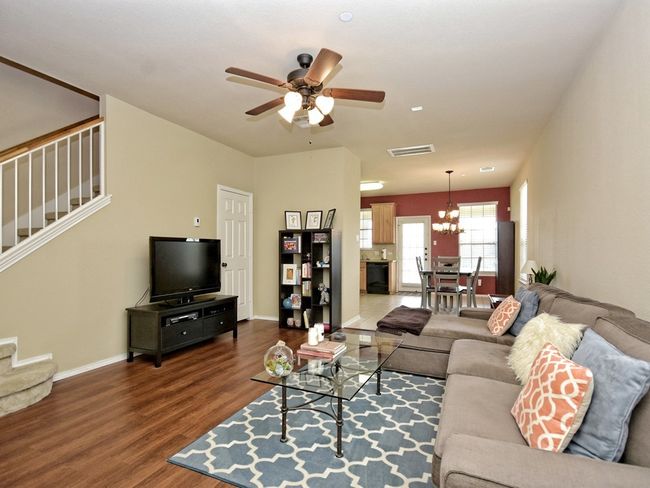 Living room with wood finished floors, stairway, and ceiling fan with notable chandelier | Image 7