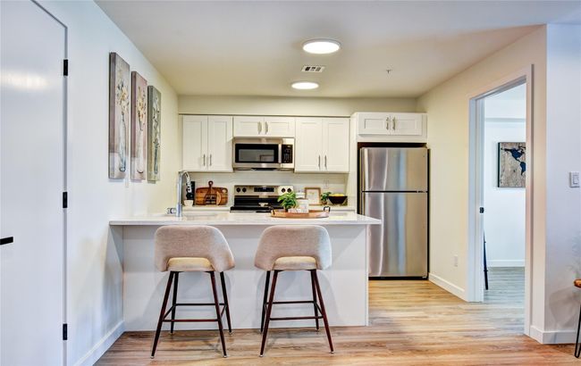 Kitchen featuring visible vents, white cabinetry, a peninsula, appliances with stainless steel finishes, and a kitchen bar | Image 8