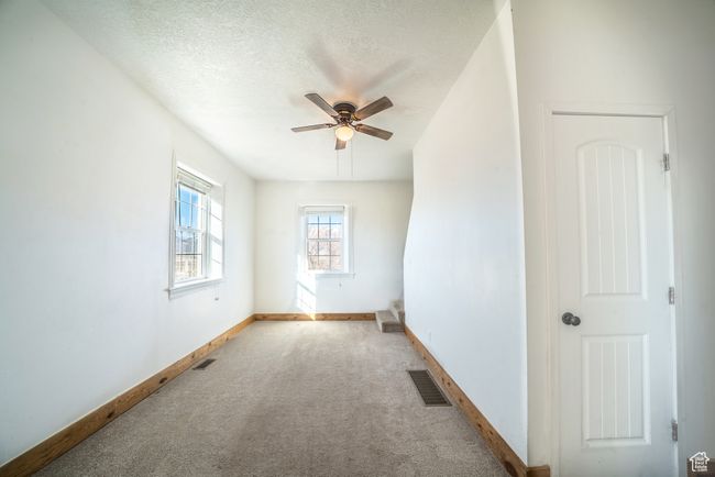 Carpeted spare room featuring a textured ceiling, a ceiling fan, visible vents, and baseboards | Image 4