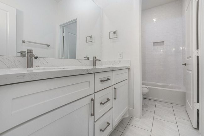 This bathroom features a modern design with a sleek double vanity, marble countertops, and chrome fixtures. It includes a spacious mirror and a tiled shower area with a built-in niche. The bright, neutral tones create a clean and inviting atmosphere. | Image 36