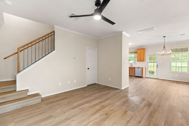 Unfurnished living room with baseboards, light wood-style floors, ceiling fan with notable chandelier, stairway, and ornamental molding | Image 10