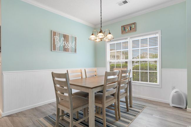 Dining area with a wainscoted wall, crown molding, light wood-style flooring, and a chandelier | Image 10