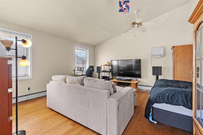 Living area with a baseboard radiator, vaulted ceiling, light wood-style flooring, and ceiling fan | Image 11