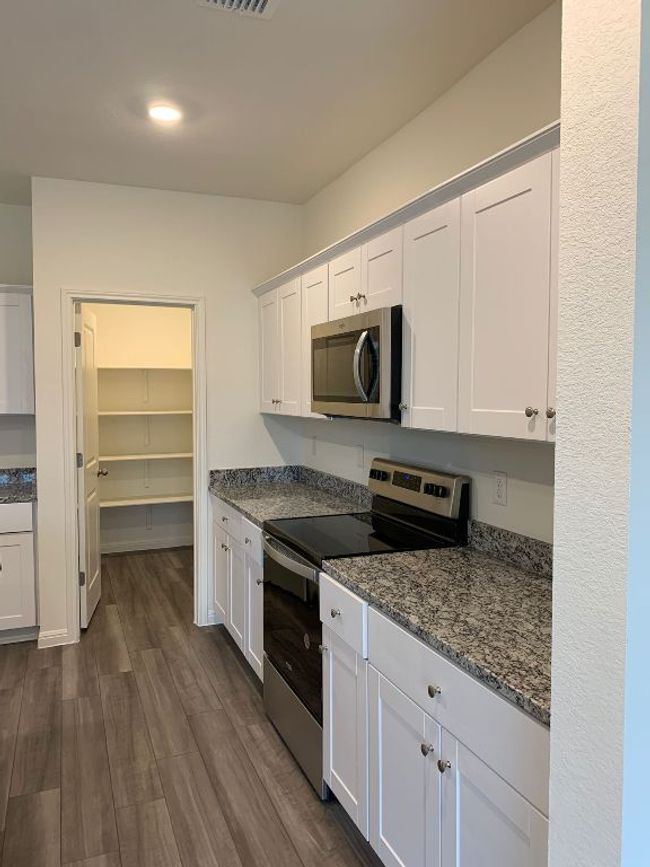 Kitchen with appliances with stainless steel finishes, dark wood-type flooring, white cabinetry, dark stone countertops, and recessed lighting | Image 4