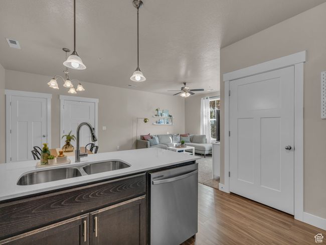 Kitchen with stainless steel dishwasher, a sink, dark brown cabinets, light wood-style floors, and pendant lighting | Image 6