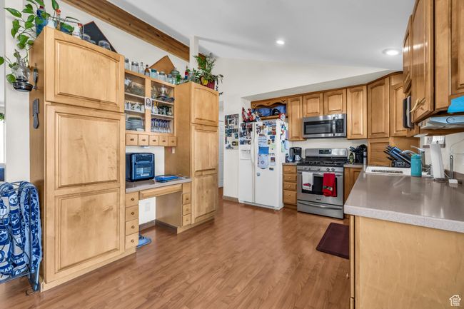 Kitchen with a sink, built in study area, light wood finished floors, appliances with stainless steel finishes, and lofted ceiling | Image 9