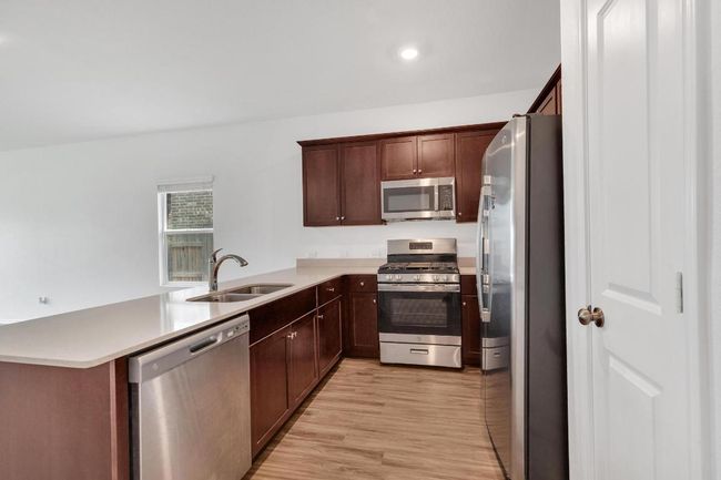 Kitchen featuring light countertops, stainless steel appliances, a sink, light wood finished floors, and a peninsula | Image 4