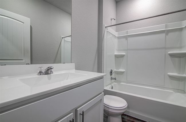 Full bath with toilet, vanity, a textured wall, and washtub / shower combination | Image 6
