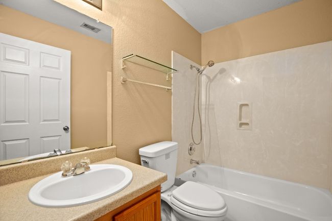 Bathroom featuring toilet, tub / shower combination, vanity, and a textured wall | Image 16