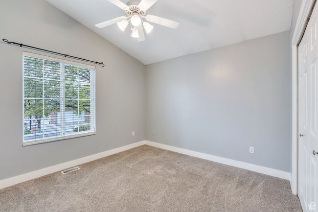 Unfurnished room with vaulted ceiling, visible vents, baseboards, light colored carpet, and ceiling fan | Image 14
