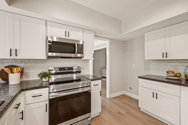 The kitchen is modern and functional with white cabinetry, stainless appliances, and dark countertops. | Image 11