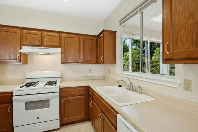 Kitchen featuring white gas range oven, under cabinet range hood, a sink, and brown cabinetry | Image 10