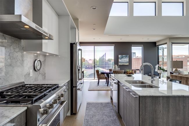 Kitchen with stainless steel appliances, a kitchen island with sink, a sink, modern cabinets, and wall chimney range hood | Image 11