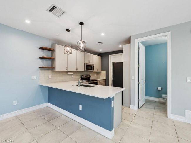 Kitchen with hanging light fixtures, stainless steel appliances, kitchen peninsula, and white cabinets | Image 4