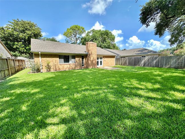Spacious backyard with lush green grass, a privacy fence, and a charming brick exterior. Ideal for outdoor activities and relaxation. | Image 13