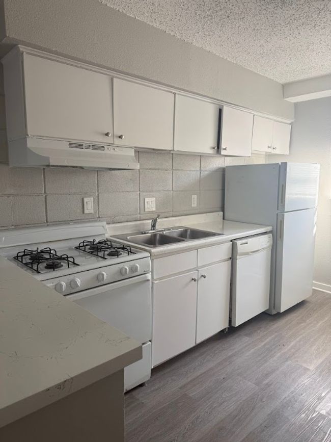 Kitchen featuring white appliances, under cabinet range hood, a sink, light wood-style floors, and light countertops | Image 7