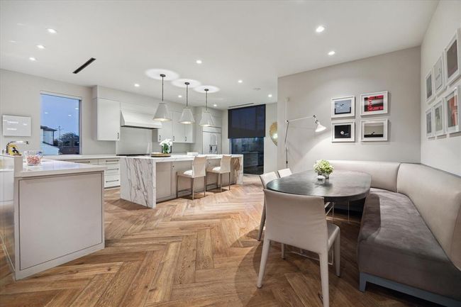 Sophisticated chef’s kitchen features a spacious breakfast nook with built-in banquette seating offering a stylish and cozy setting for casual dining. The open layout, designer lighting, and that gorgeous herringbone wood flooring complete this modern culinary haven. | Image 9