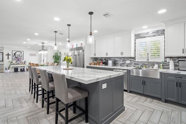 Kitchen with gray cabinets, backsplash, appliances with stainless steel finishes, a center island, and visible vents | Image 4