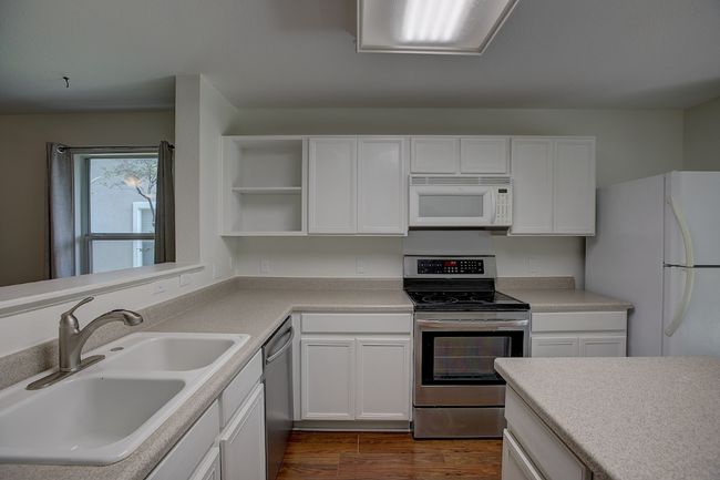 Kitchen with stainless steel appliances, a sink, open shelves, and white cabinets | Image 19