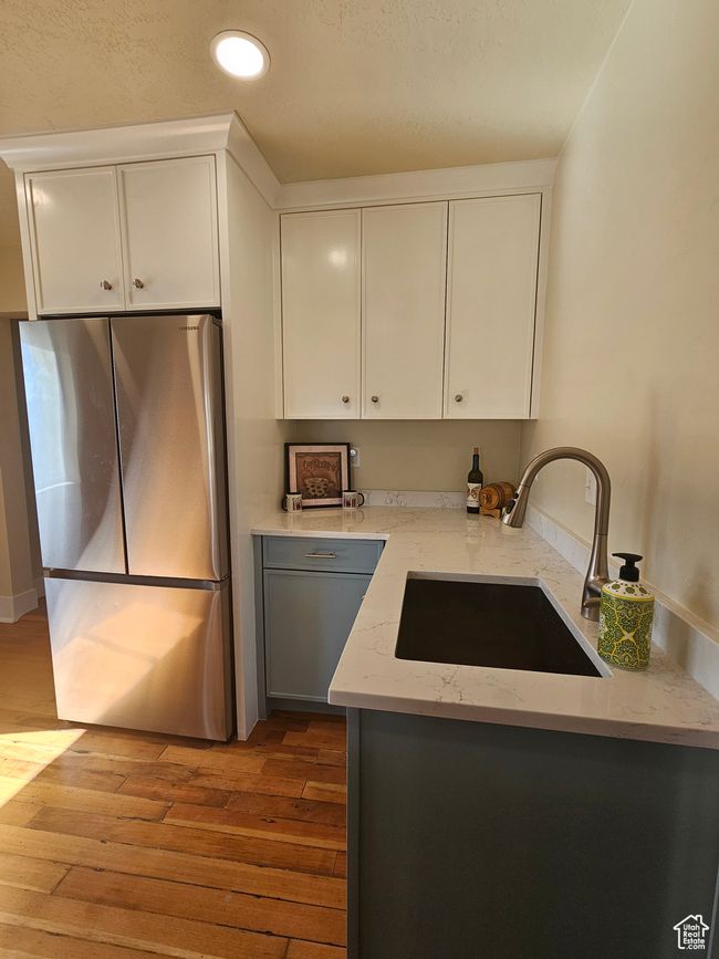 Kitchen featuring freestanding refrigerator, a sink, wood finished floors, custom cabinetry, and quartz countertops | Image 13