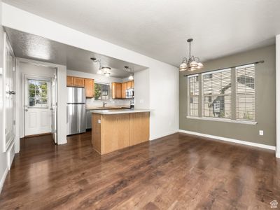 Kitchen with dark wood-type flooring, kitchen peninsula, pendant lighting, stainless steel appliances, and a notable chandelier | Image 3