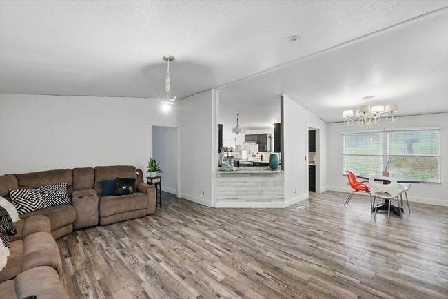 Living room featuring vaulted ceiling, wood finished floors, a chandelier, and baseboards | Image 4