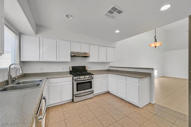 Kitchen with gas stove, under cabinet range hood, white cabinetry, a peninsula, and recessed lighting | Image 6