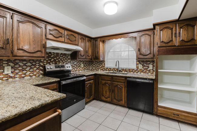 Kitchen with stainless steel electric range, under cabinet range hood, a sink, light tile patterned flooring, and dishwasher | Image 7