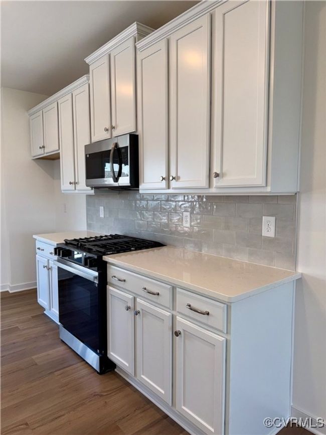 Kitchen featuring white cabinets, wood finished floors, stainless steel microwave, gas stove, and tasteful backsplash | Image 6