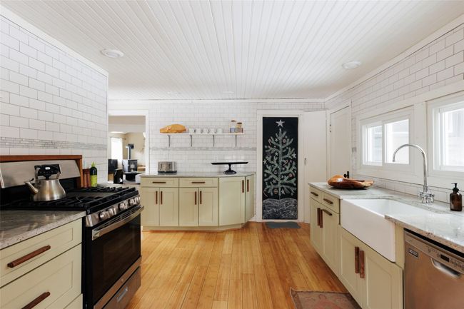 Kitchen featuring light stone counters, stainless steel appliances, cream cabinetry, and light wood-type flooring | Image 17