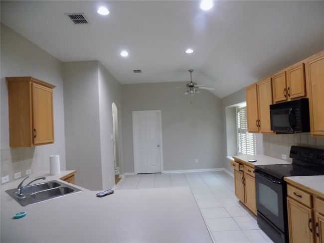 Kitchen with black appliances, ceiling fan, backsplash, light tile patterned floors, and light countertops | Image 16