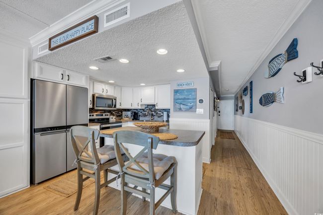 Kitchen featuring appliances with stainless steel finishes, a textured ceiling, white cabinetry, wainscoting, and light wood-style floors | Image 18