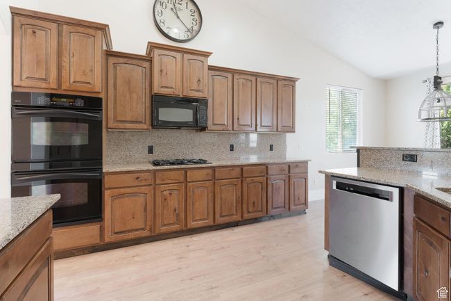 Kitchen featuring black appliances, lofted ceiling, backsplash, light wood-style flooring, and light stone countertops | Image 15