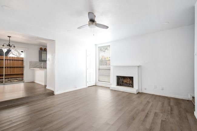 Unfurnished living room featuring a brick fireplace, wood-type flooring, ceiling fan with notable chandelier, and plenty of natural light | Image 5