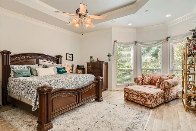 Bedroom featuring light wood finished floors, a raised ceiling, ceiling fan, and ornamental molding | Image 18