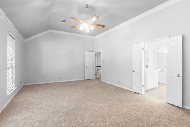 Unfurnished bedroom featuring light colored carpet, crown molding, multiple windows, lofted ceiling, and baseboards | Image 26