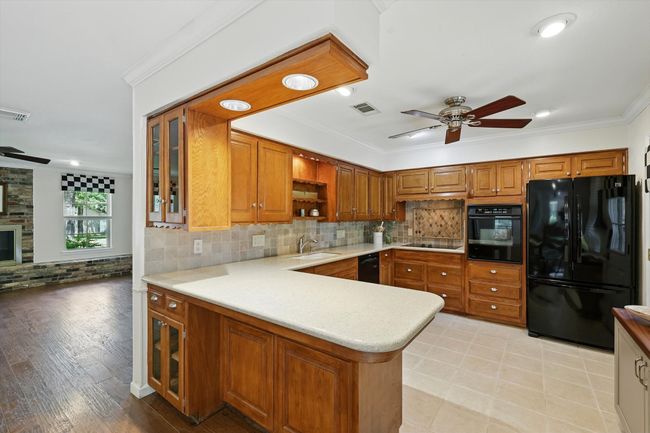 Kitchen featuring black appliances, ceiling fan, a peninsula, brown cabinets, and crown molding | Image 10