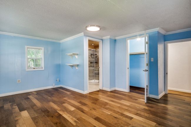 Unfurnished bedroom featuring hardwood / wood-style flooring, a textured ceiling, ornamental molding, ensuite bath, and a closet | Image 20