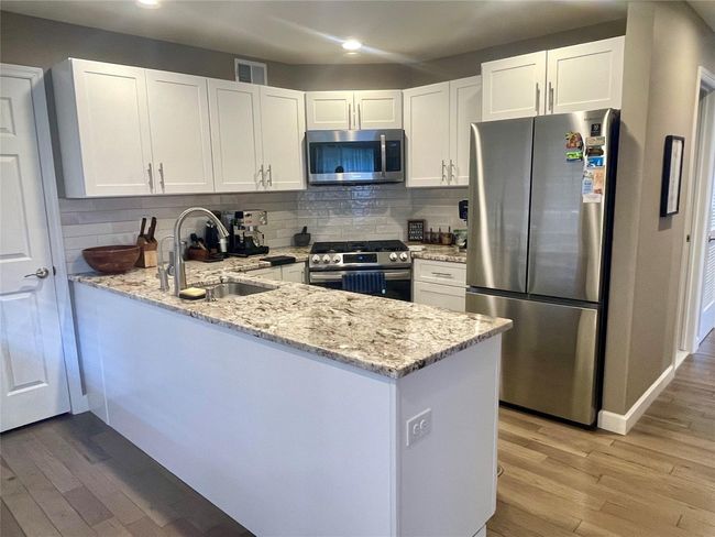 Kitchen featuring light wood-type flooring, stainless steel appliances, a sink, and light stone counters | Image 14
