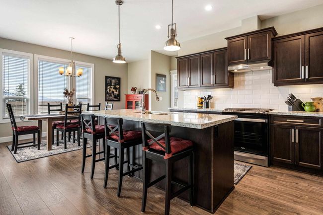 Kitchen with backsplash, stainless steel gas range oven, under cabinet range hood, a kitchen island with sink, and dark wood-type flooring | Image 4