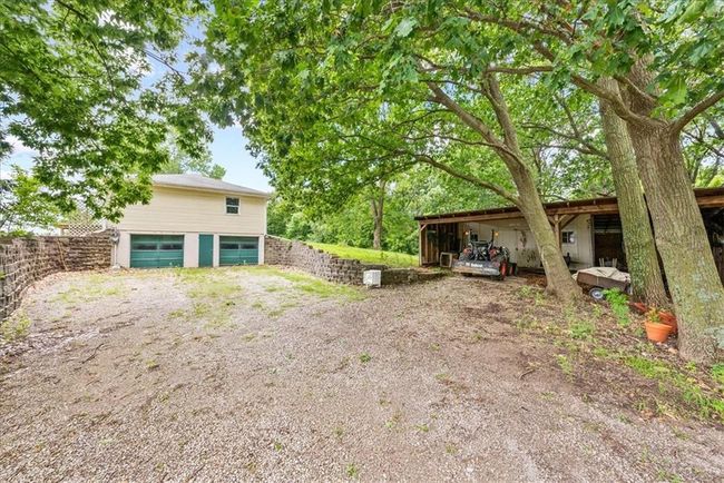 Back of house featuring an outbuilding, fence, an outdoor structure, an attached garage, and dirt driveway | Image 64