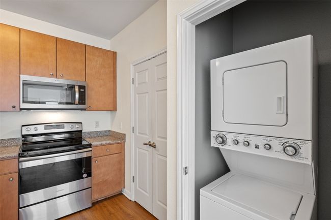 Kitchen with stainless steel appliances, brown cabinets, light wood-style flooring, stacked washer and clothes dryer, and light stone countertops | Image 11
