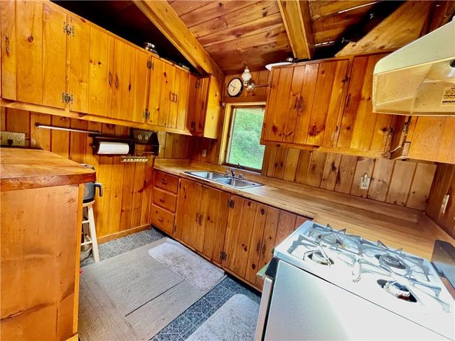 Kitchen featuring range, wooden walls, sink, beam ceiling, and range hood | Image 4