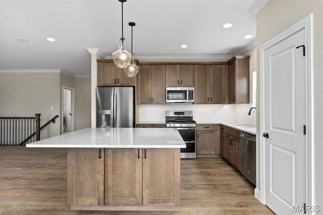 Kitchen with appliances with stainless steel finishes, a sink, light wood finished floors, a center island, and ornamental molding | Image 14
