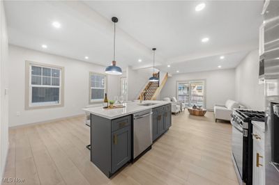 Kitchen with appliances with stainless steel finishes, hanging light fixtures, a center island with sink, and light hardwood / wood-style flooring | Image 2